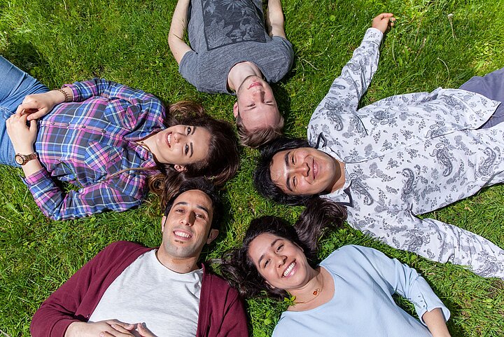 Grupa młodych ludzi leżących na trawie stykając się głowami