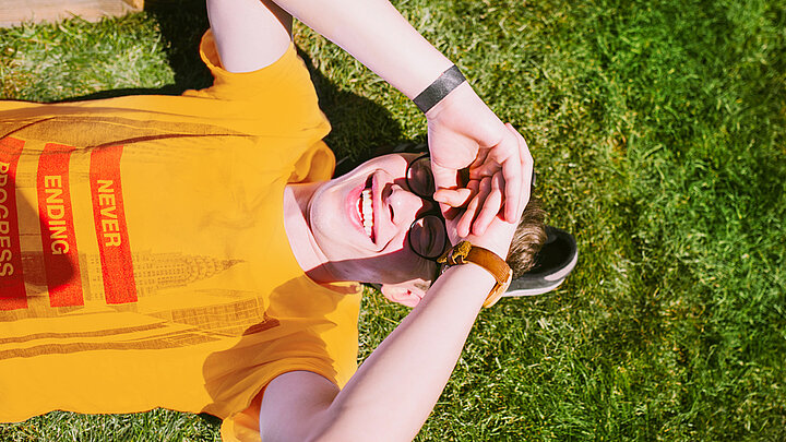 A picture of a young man lying on the grass with his hand on his forehead